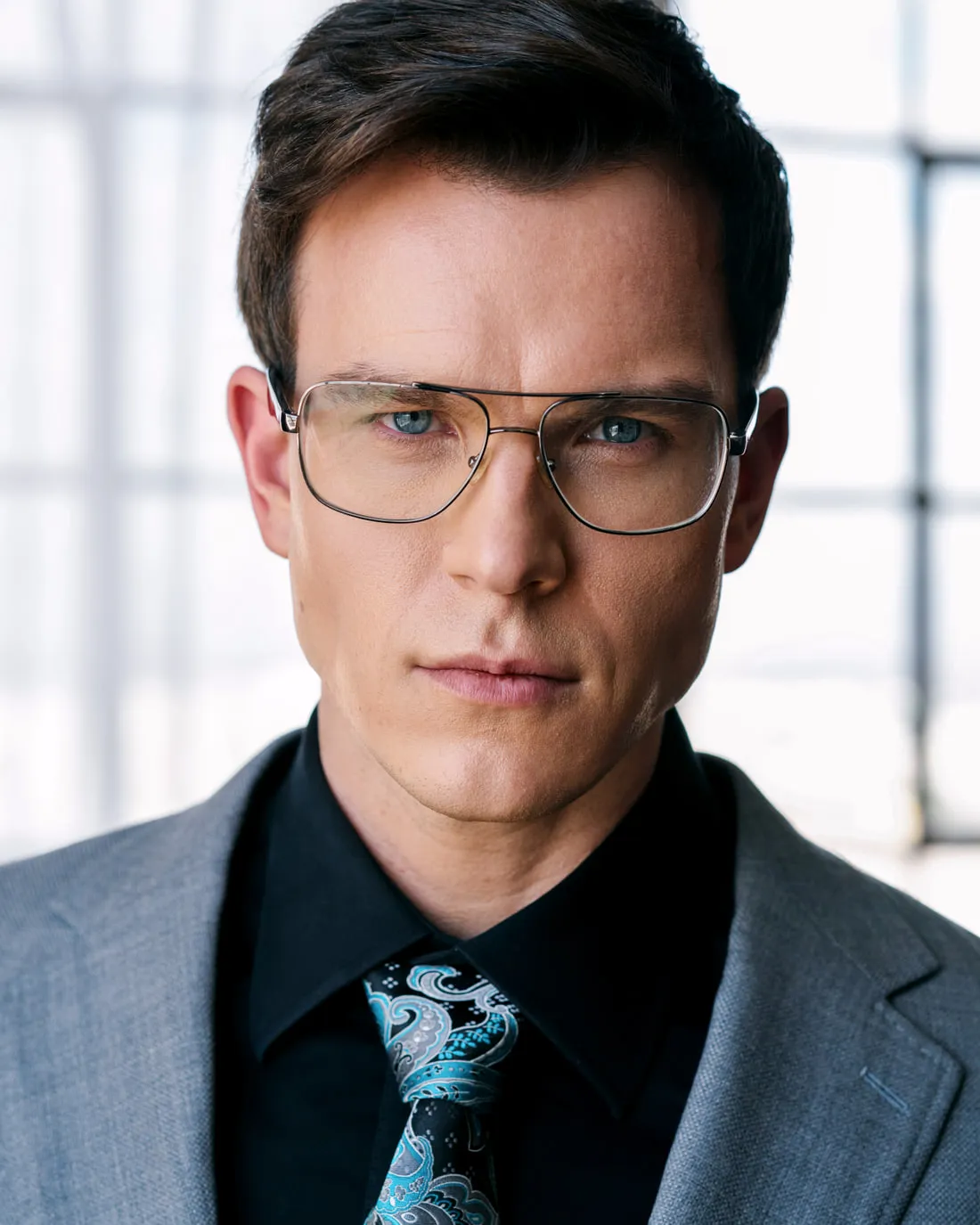 Steven Roderick Jurich in a grey suit, black shirt and wire-framed glasses