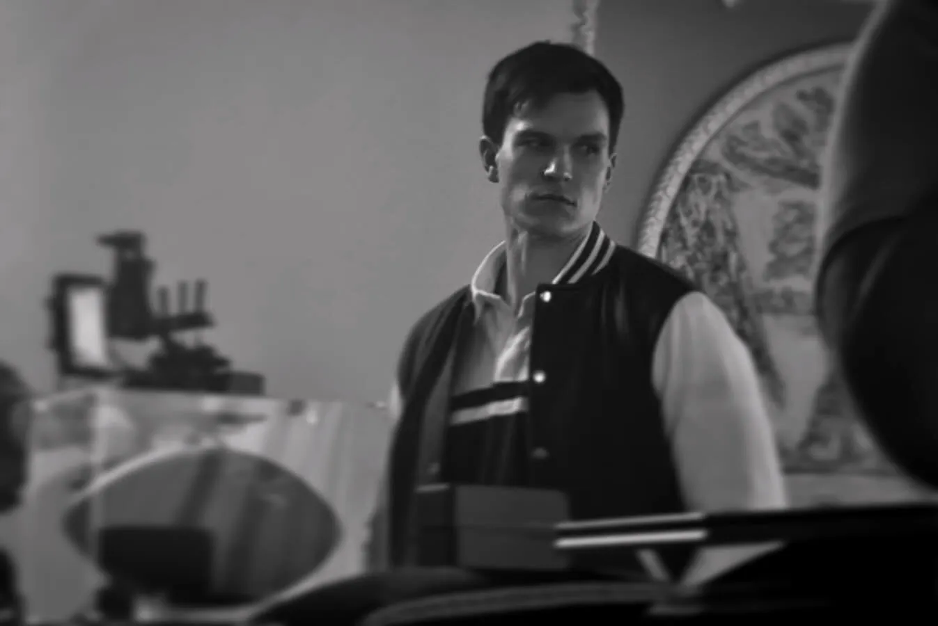 Black and white — seated at a desk under a lamp, mid-scene