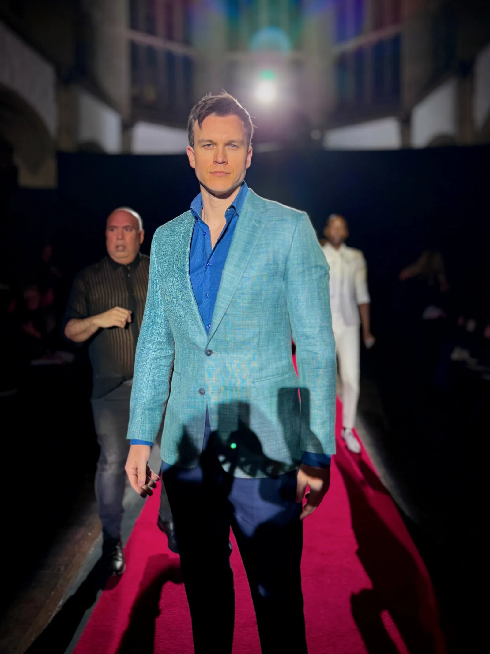 Steven Roderick Jurich on the runway in a pale blue blazer under stage light