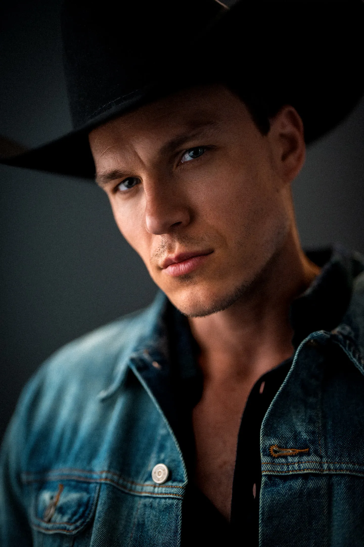 Steven Roderick Jurich in a black cowboy hat and open denim shirt, low key lighting