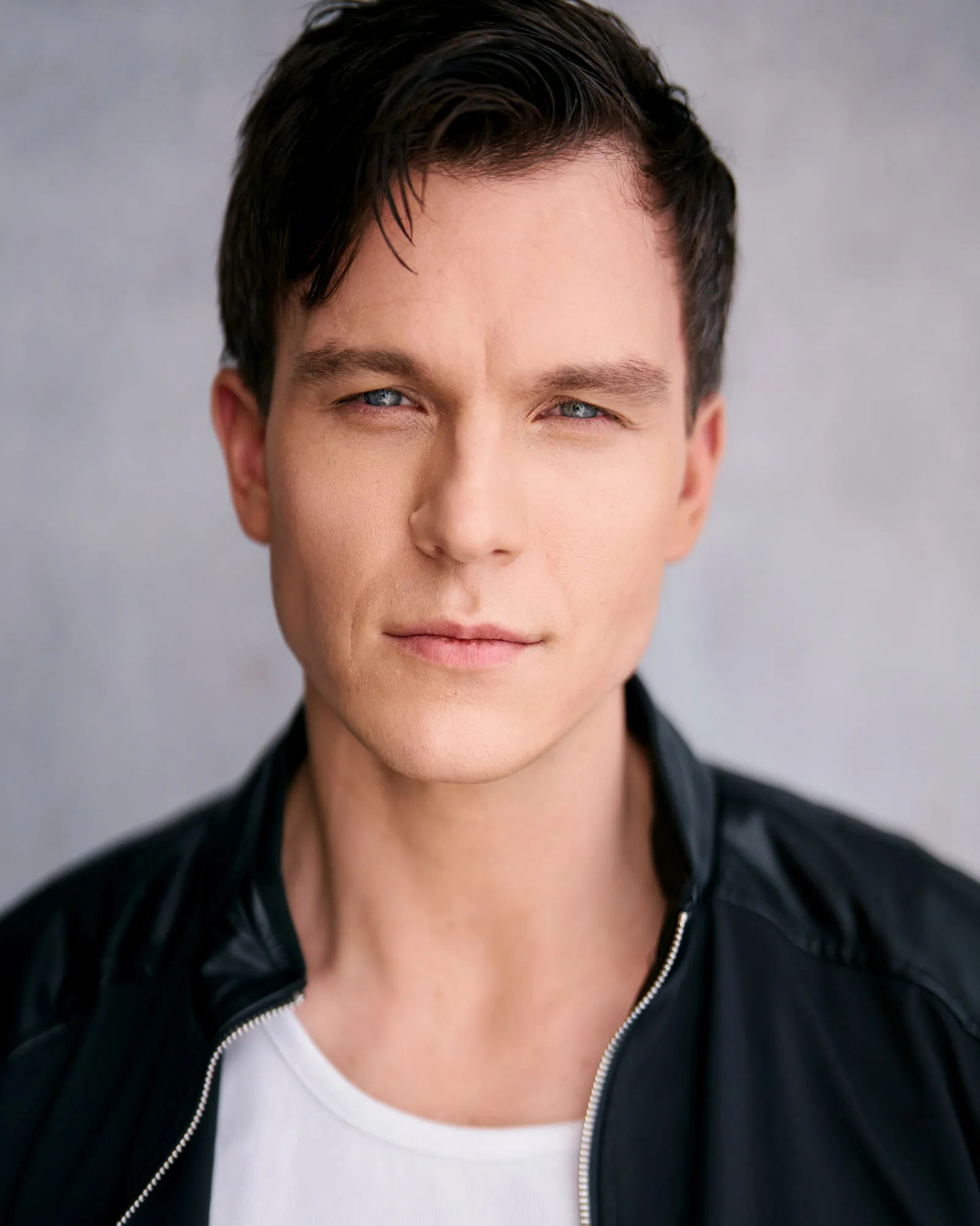 Steven Roderick Jurich in a black bomber jacket over a white tee, grey backdrop