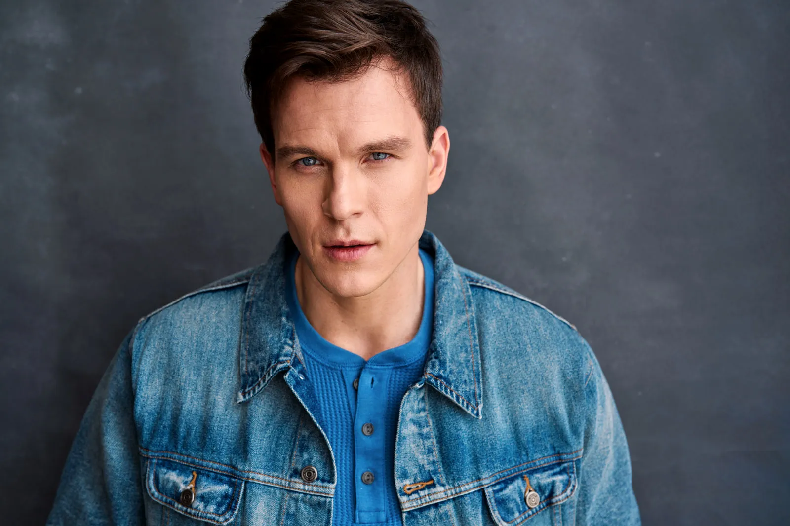 Steven Roderick Jurich against a sunlit concrete wall in a leather jacket